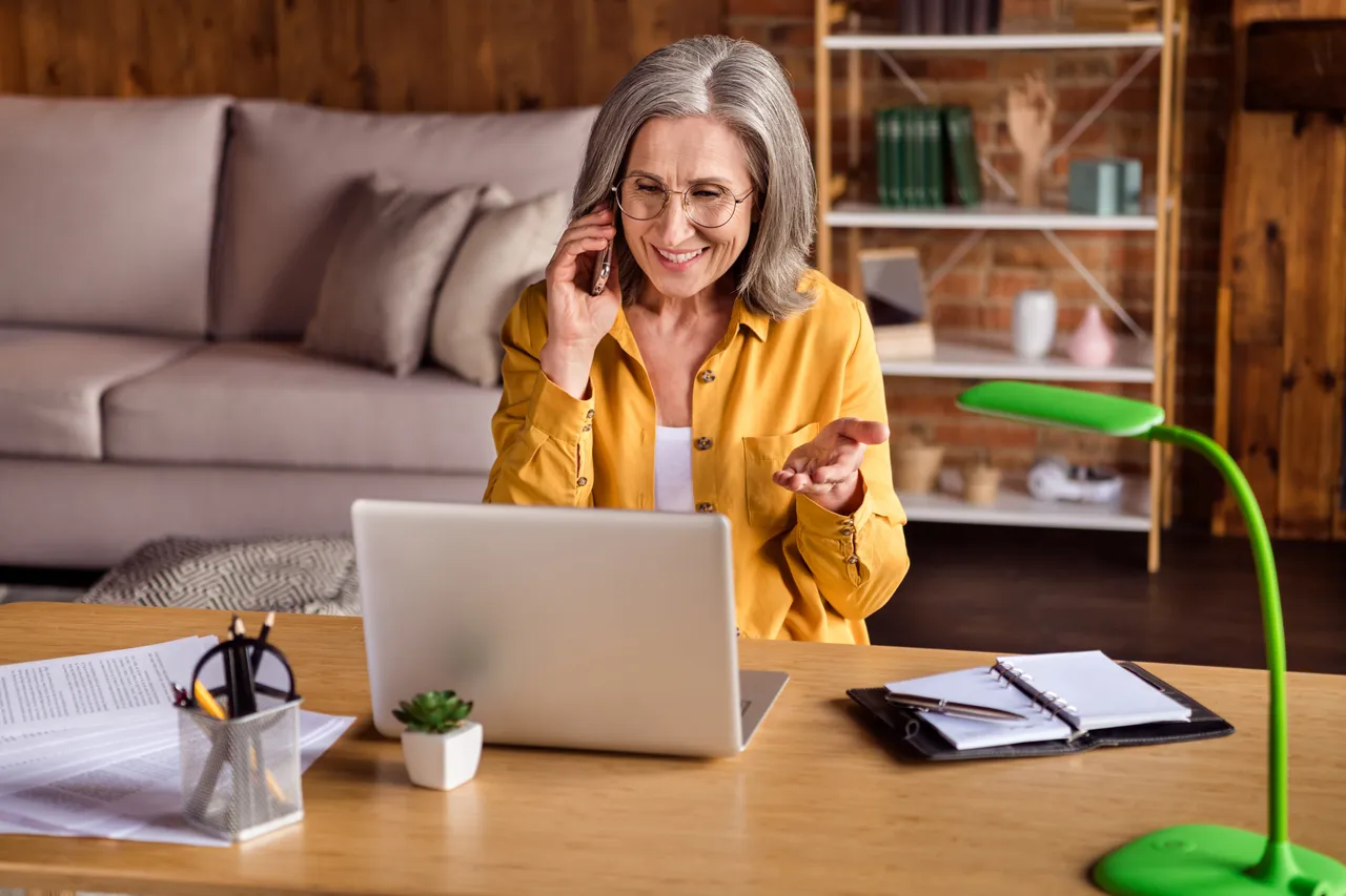 A business woman working from home with laptop talking over the phone and smiling